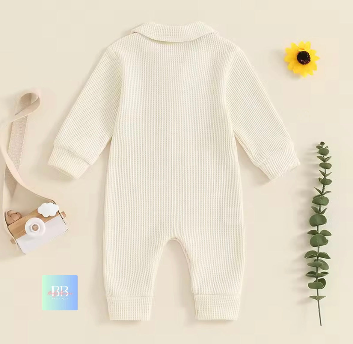 Baby onesie on a beige background with a sunflower and eucalyptus leaf