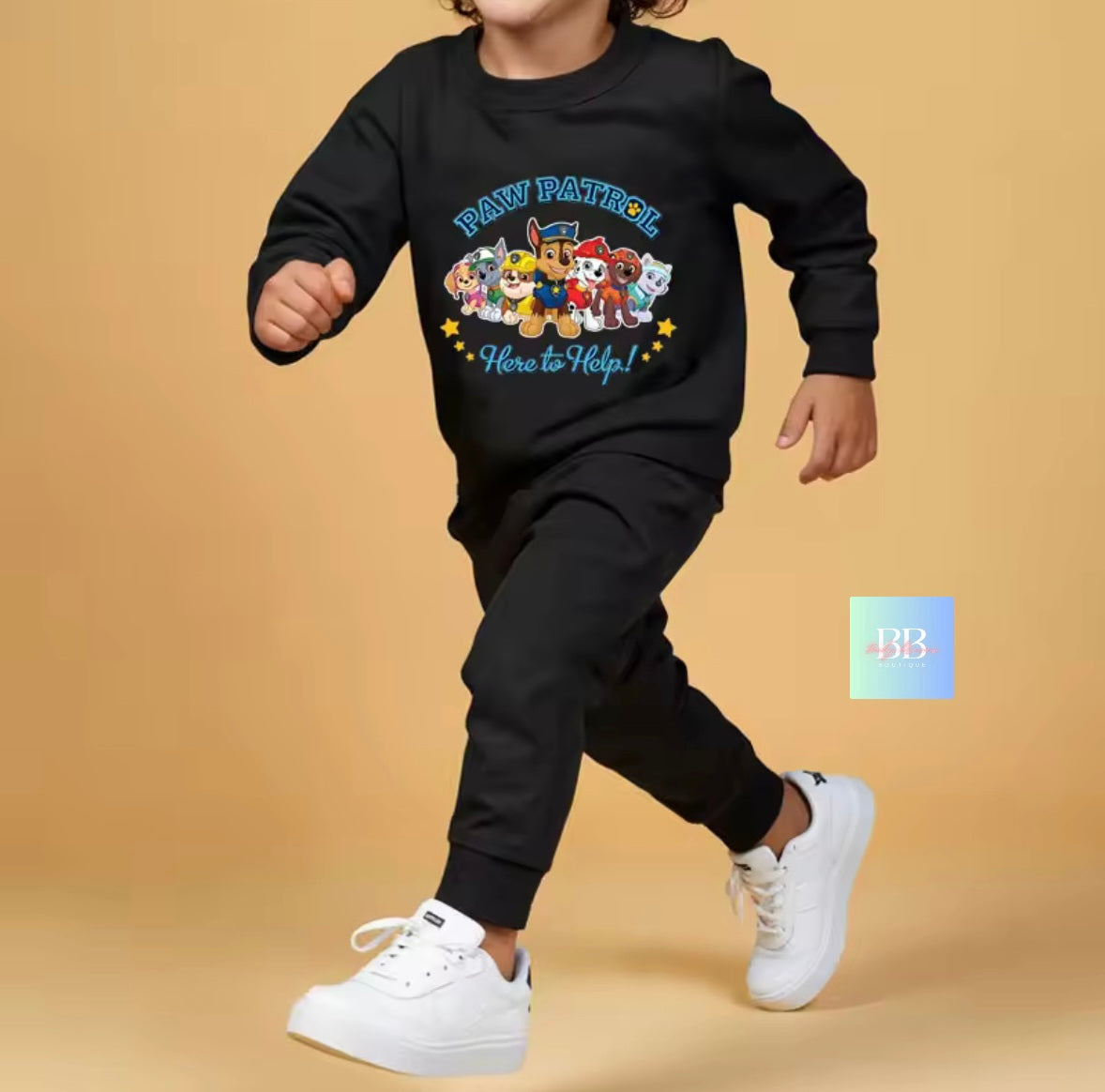 Child wearing a black 'Paw Patrol' sweatshirt and pants with white shoes on a beige background
