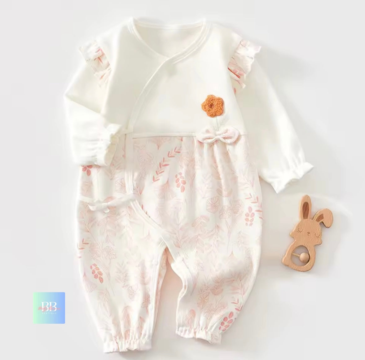 Baby romper with floral design and wooden toy on a white background