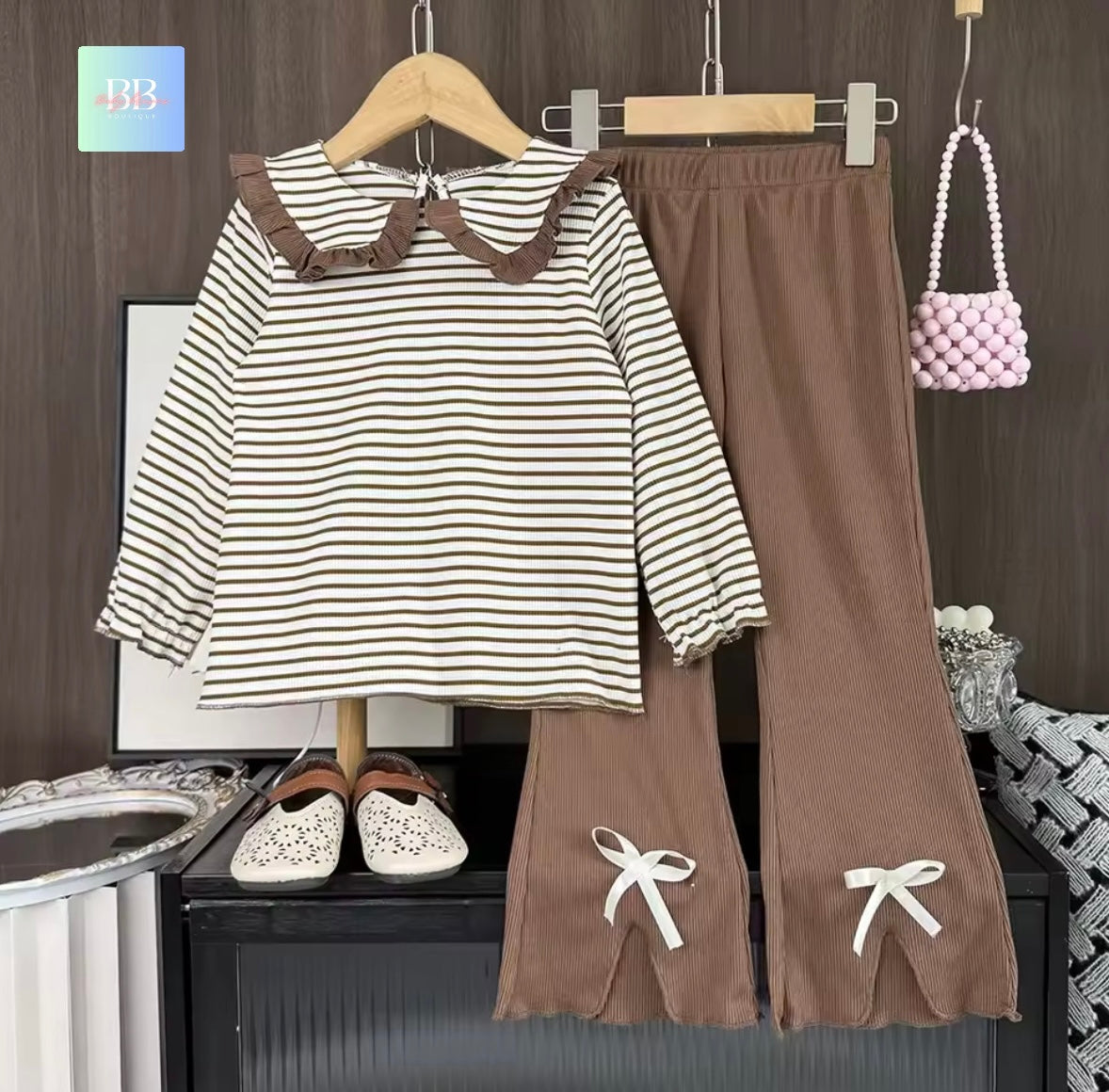 Striped shirt and brown pants with decorative elements on a wooden hanger against a dark background.