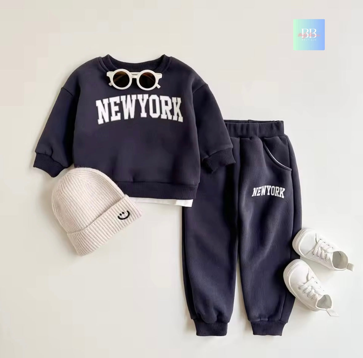 Navy blue 'New York' sweatshirt and pants with a white beanie and shoes on a light gray background