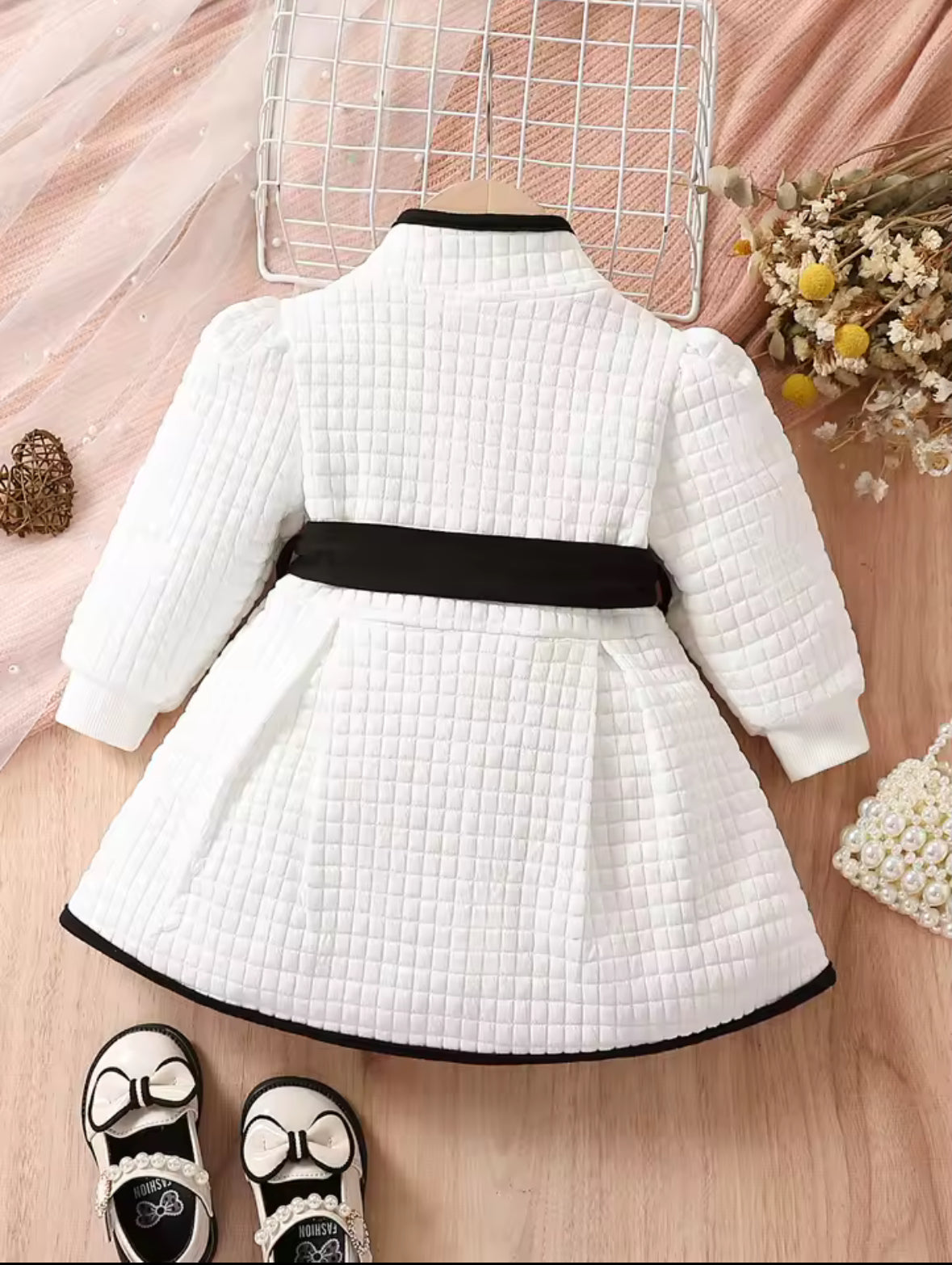 White quilted dress with a black belt on a wooden floor with decorative elements.