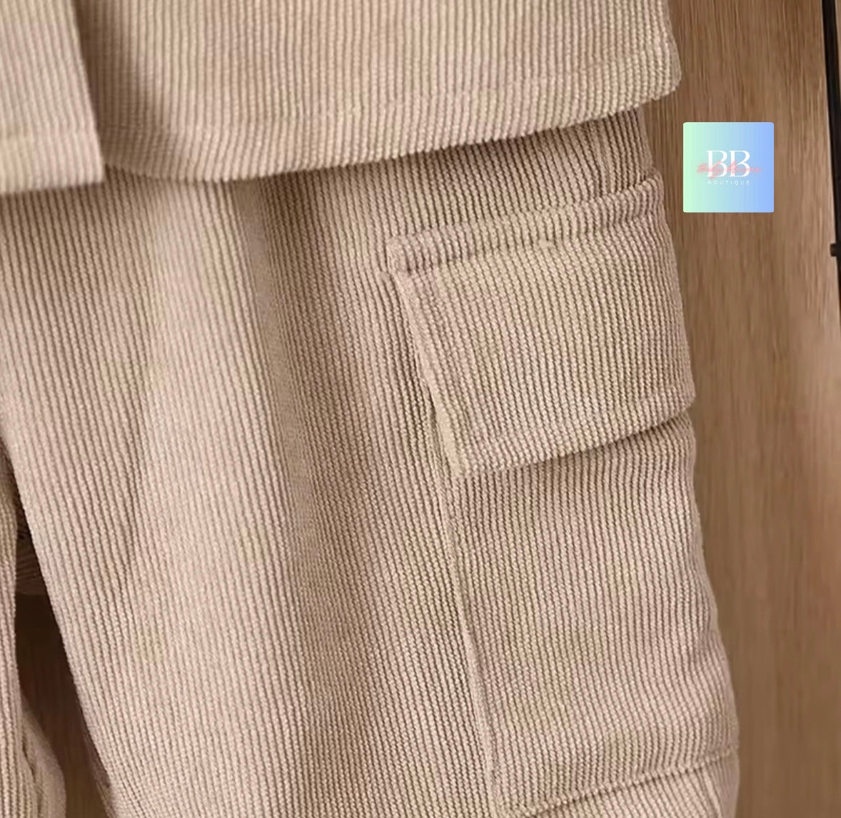 Beige corduroy pants with a pocket detail on a wooden floor.