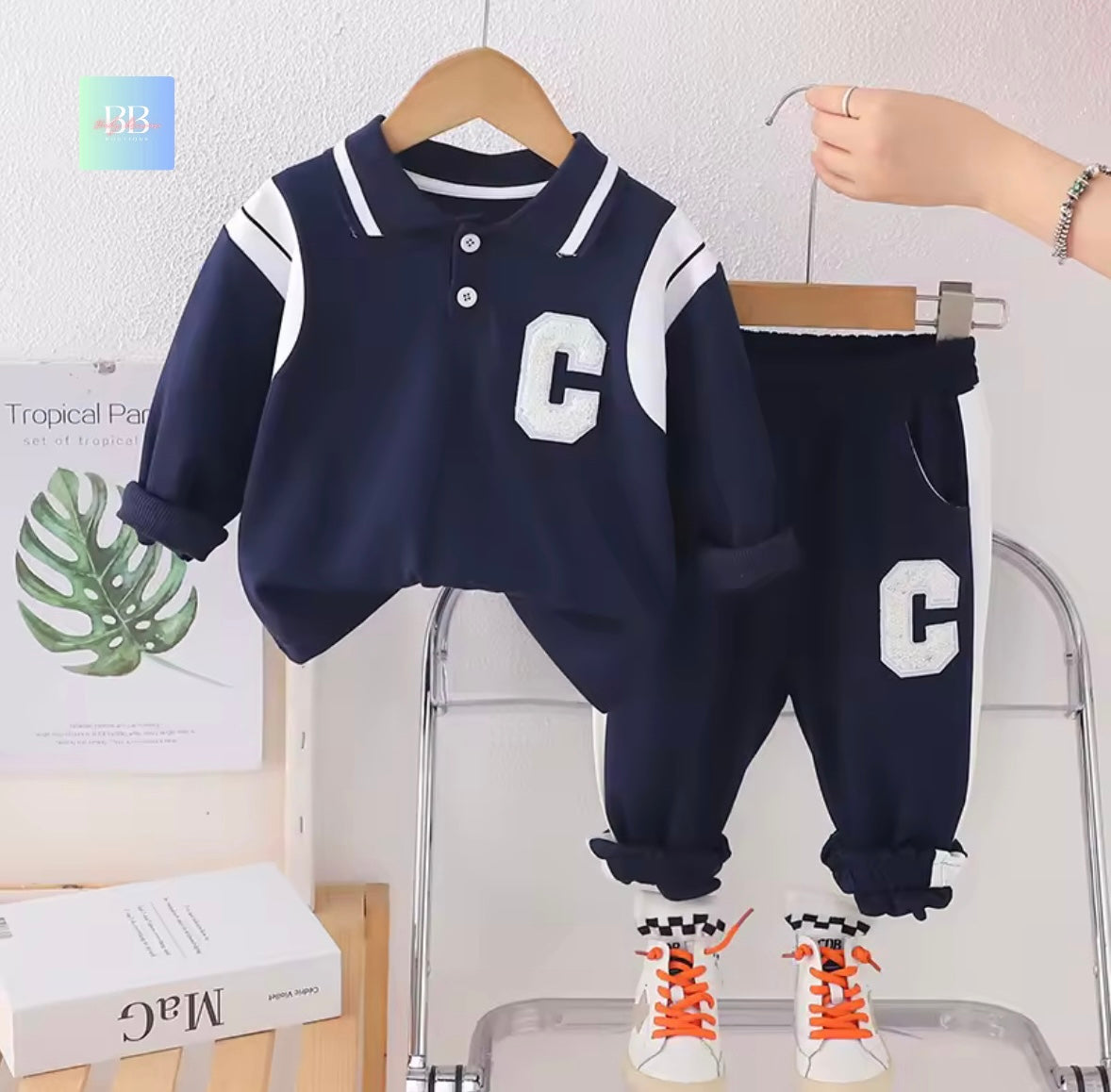 Children's navy blue and white outfit with 'C' logo on a hanger against a white wall.