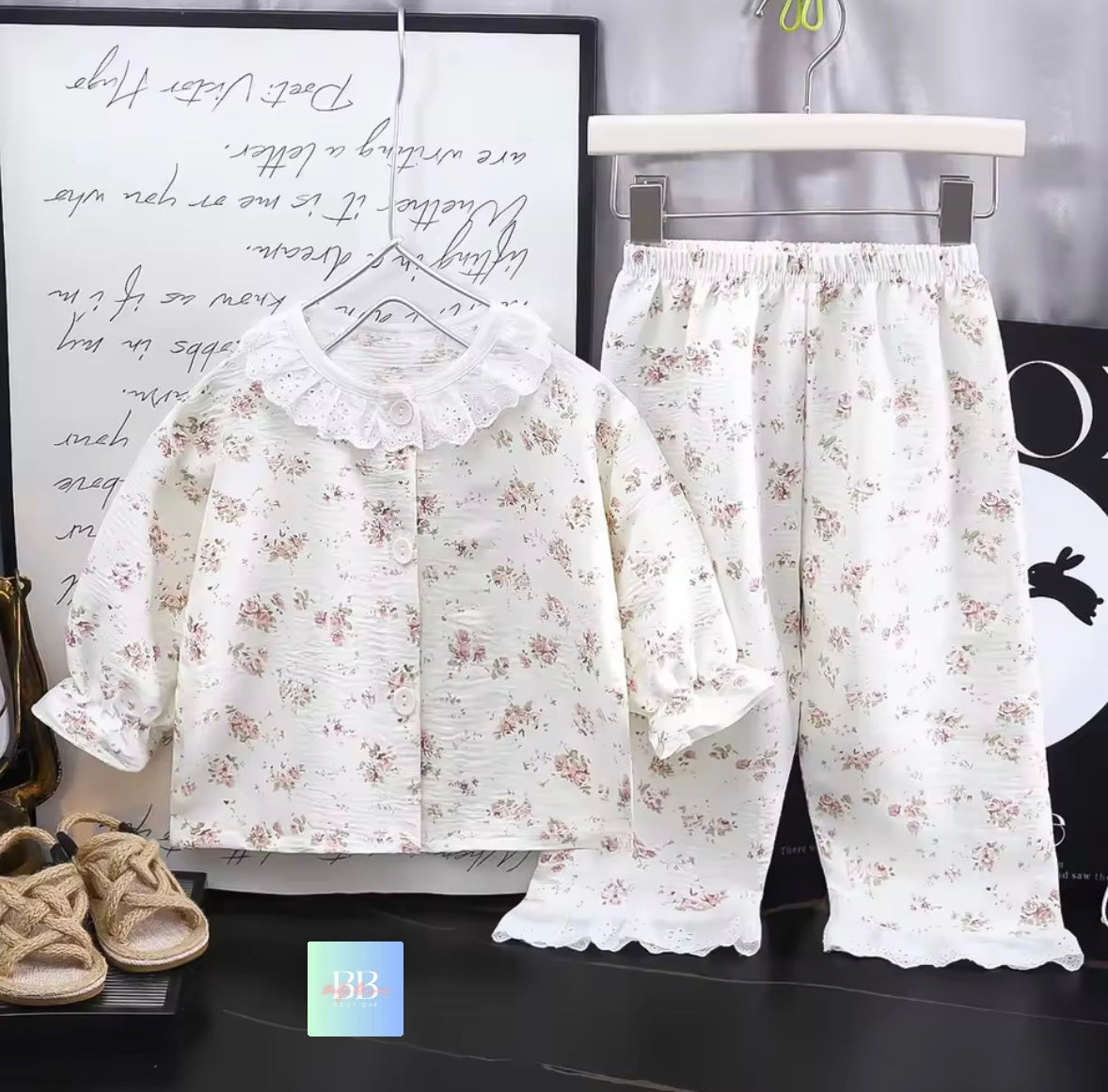 Floral pajama set with a shirt and pants on hangers against a decorative wall.