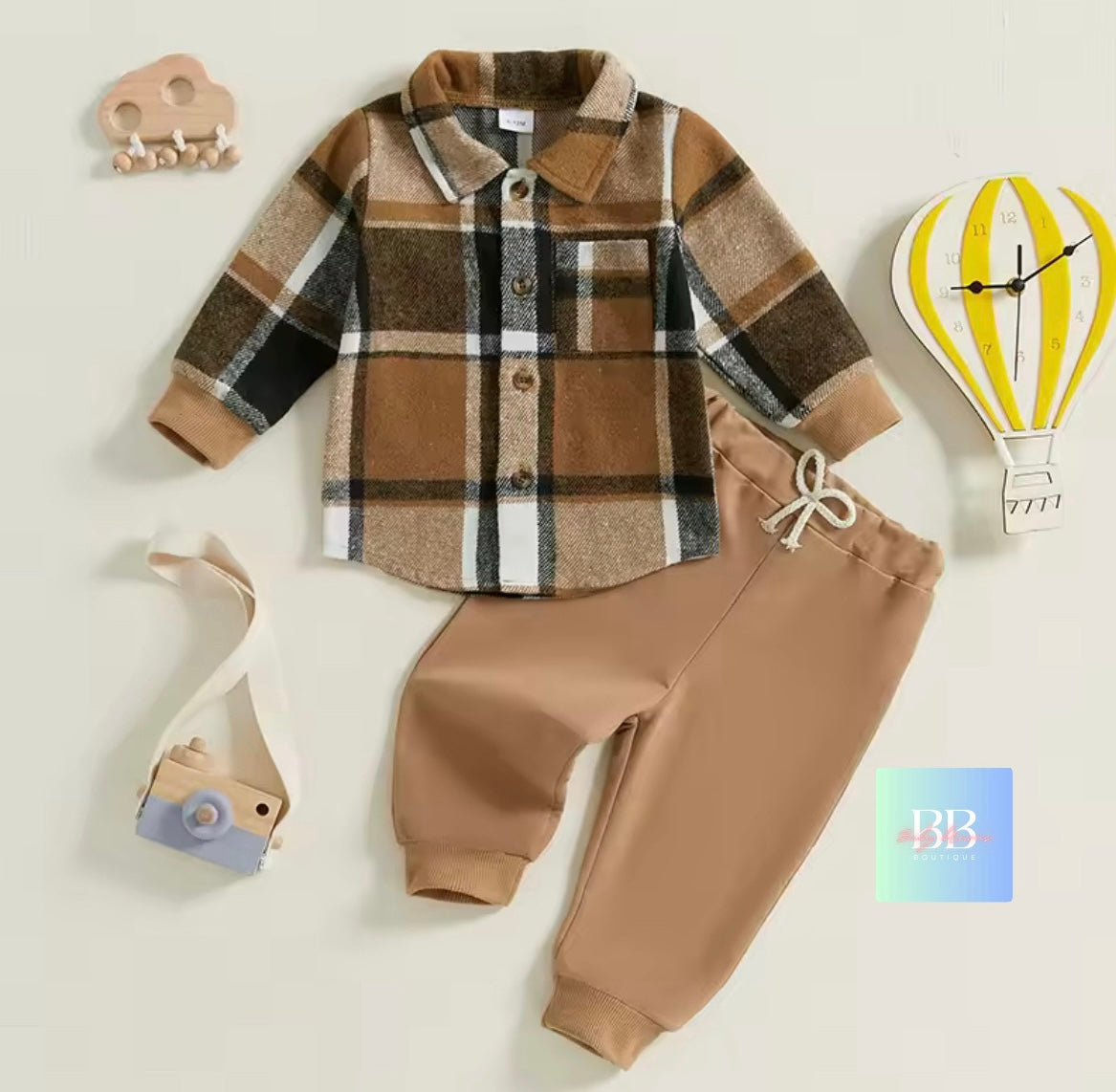 Children's plaid shirt and brown pants set on a light background with decorative items.