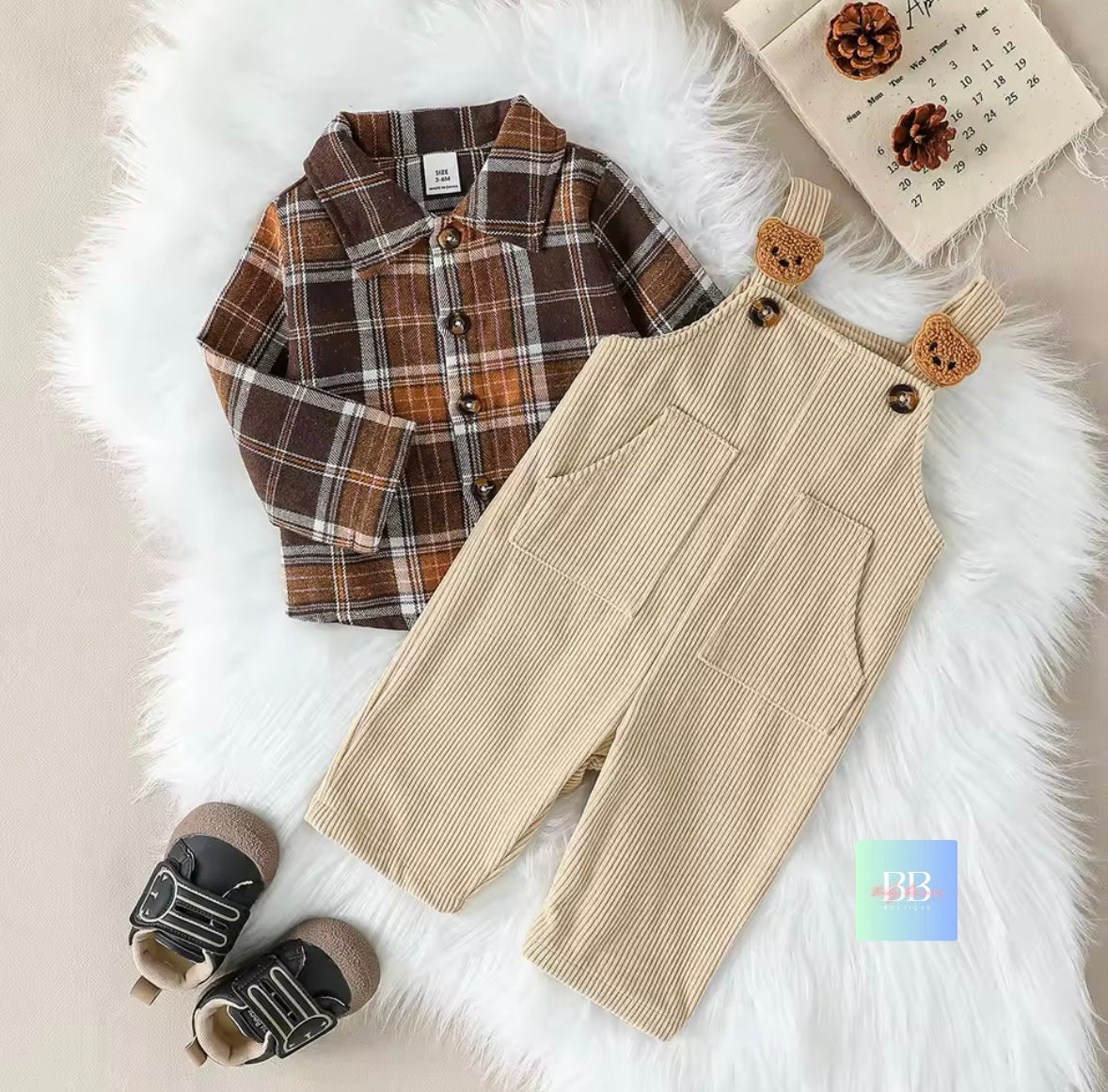 Children's plaid shirt and beige overalls with bear ears on a fluffy white surface.