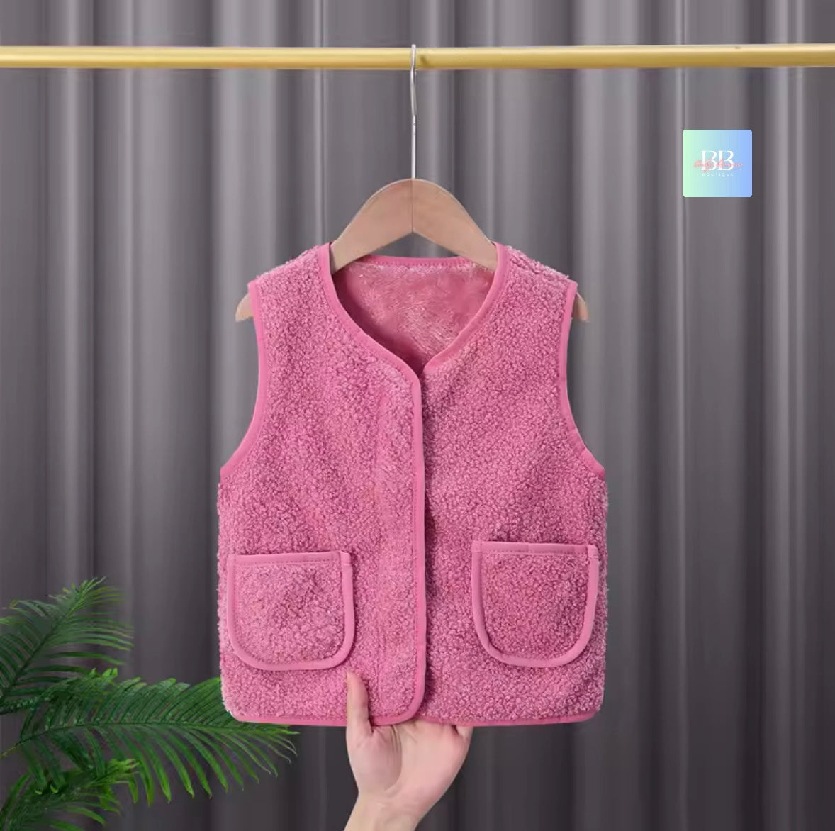 Pink fleece vest on a hanger against a gray curtain background