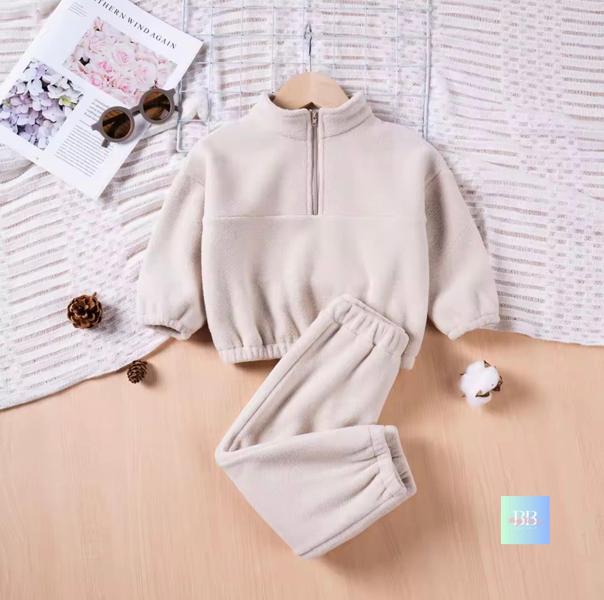 Children's beige fleece set on a wooden surface with a textured fabric background