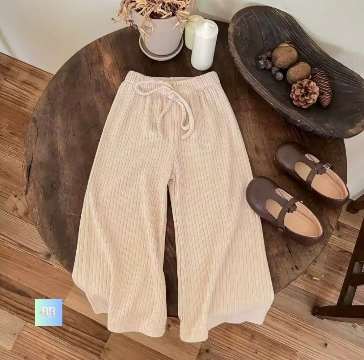 Beige pants on a wooden table with shoes and decor items.