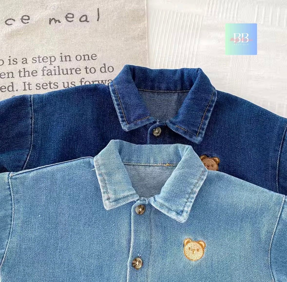 Two denim jackets with bear embroidery on a textured surface.