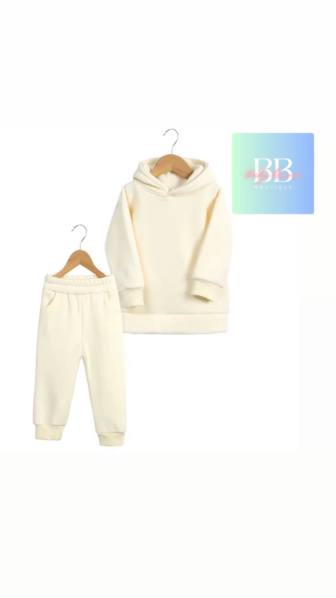 Cream-colored hoodie and jogger pants set on hangers with a brand logo in the corner.