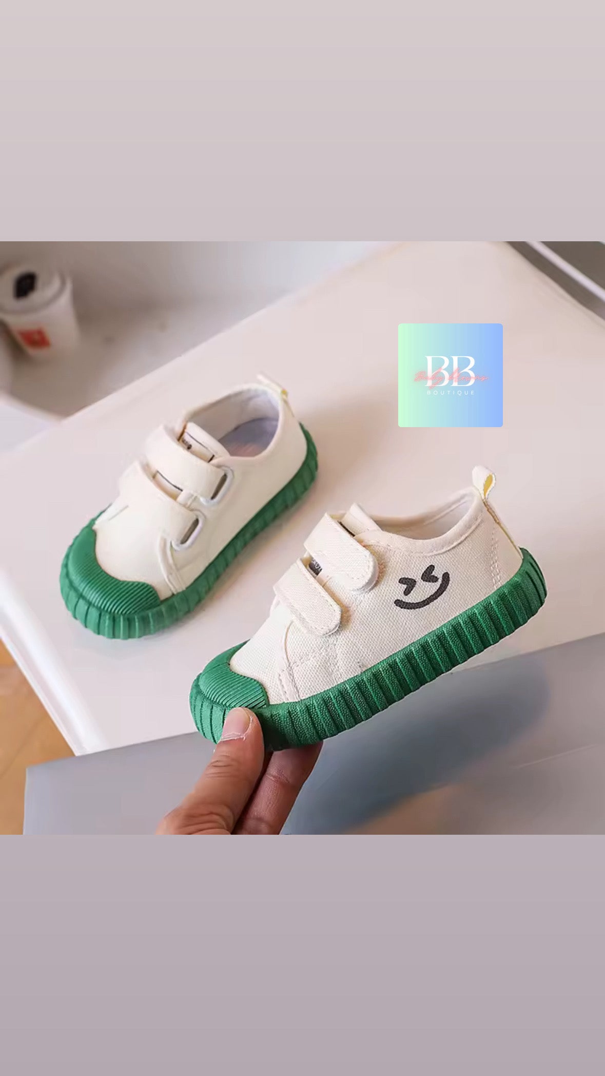 White sneakers with green soles held by a hand on a light background
