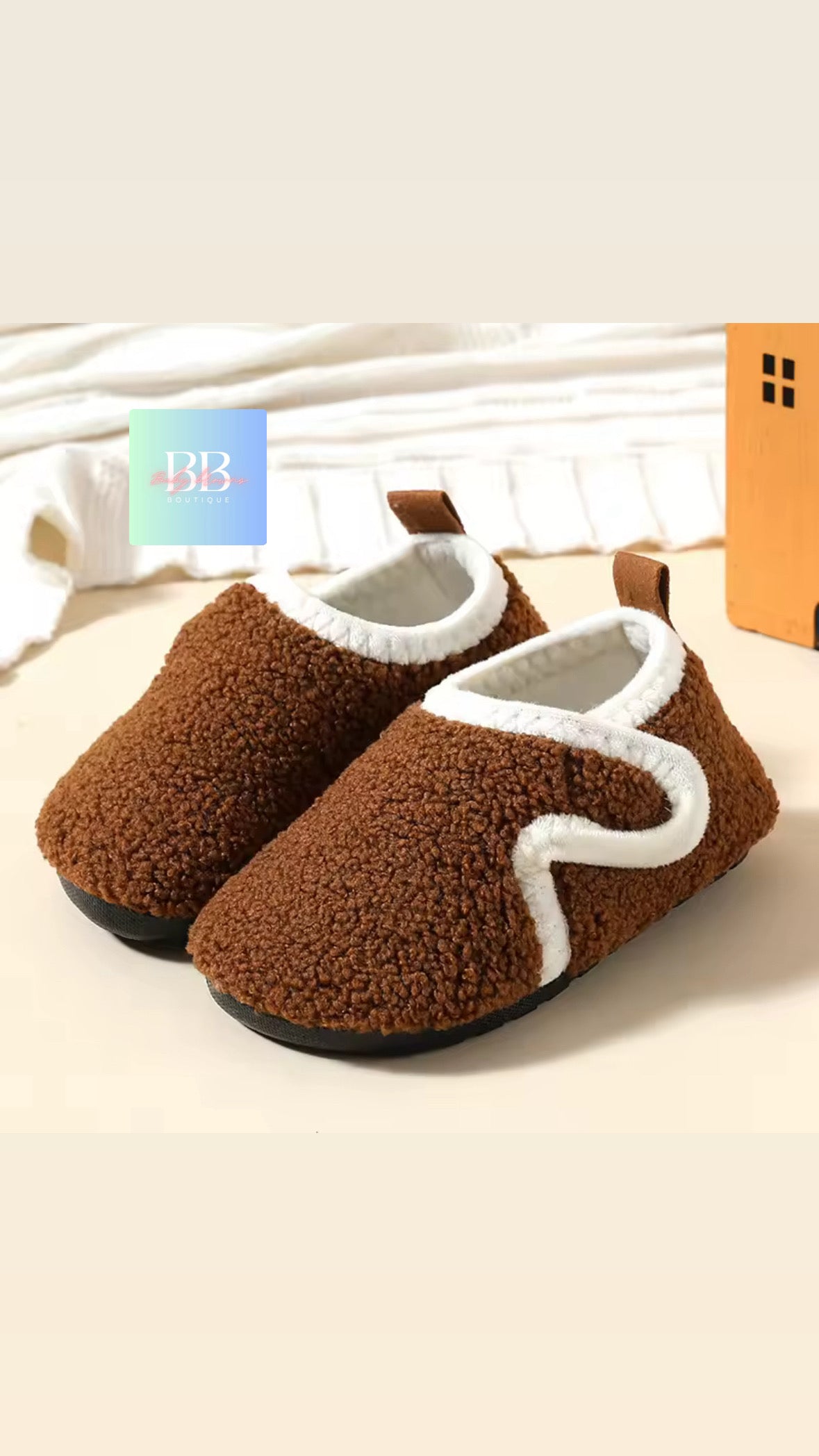 Brown fuzzy slippers with white accents on a light background