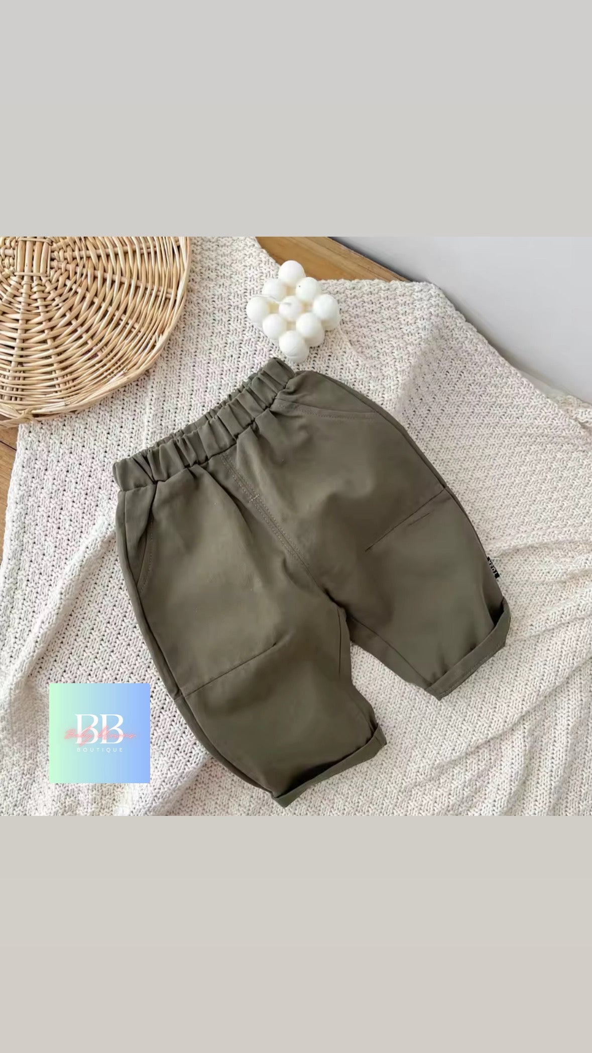 Green baby pants on a textured surface with a woven basket and white balls in the background.