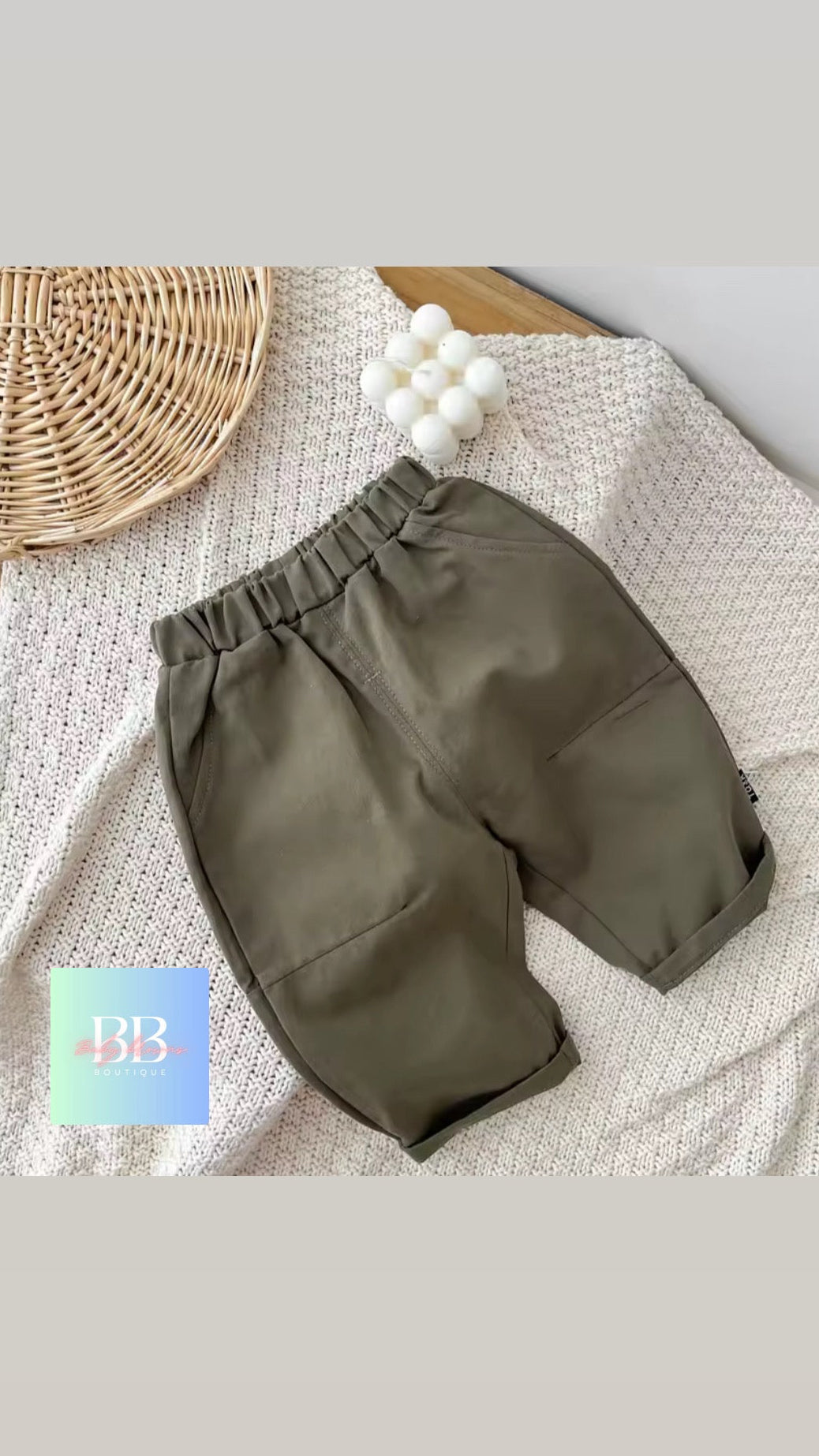 Green baby pants on a textured surface with a woven basket and white balls in the background.