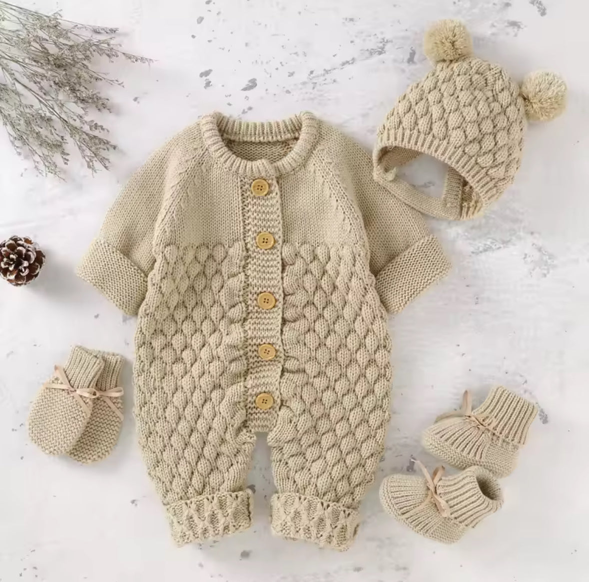 Knitted baby romper with hat, mittens, and booties on a light background