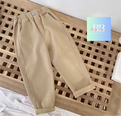 Beige pants on a wooden surface with a brand logo in the corner.