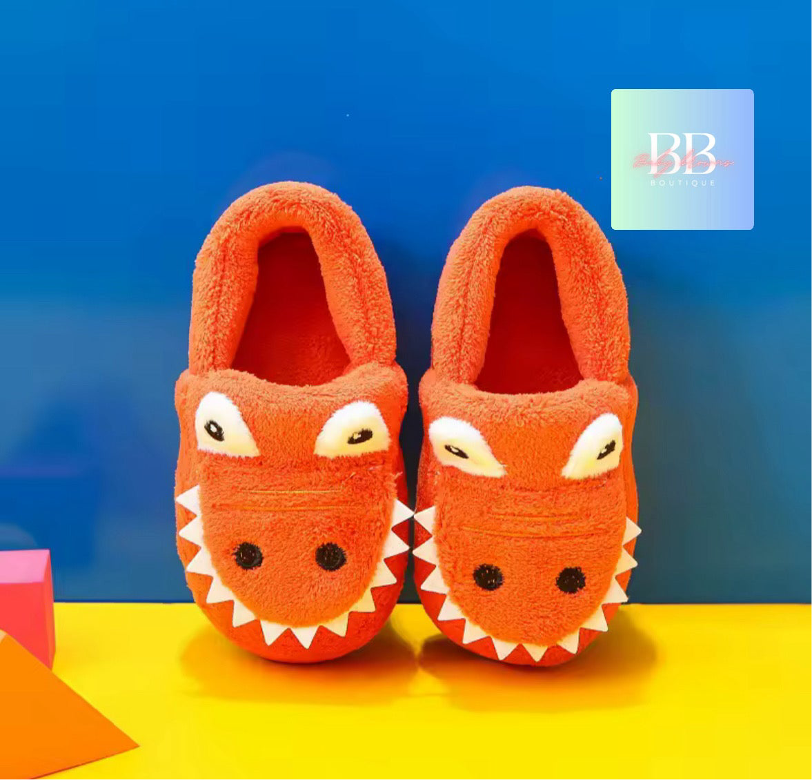 Pair of orange children's slippers with fox design on a blue and yellow gradient background.