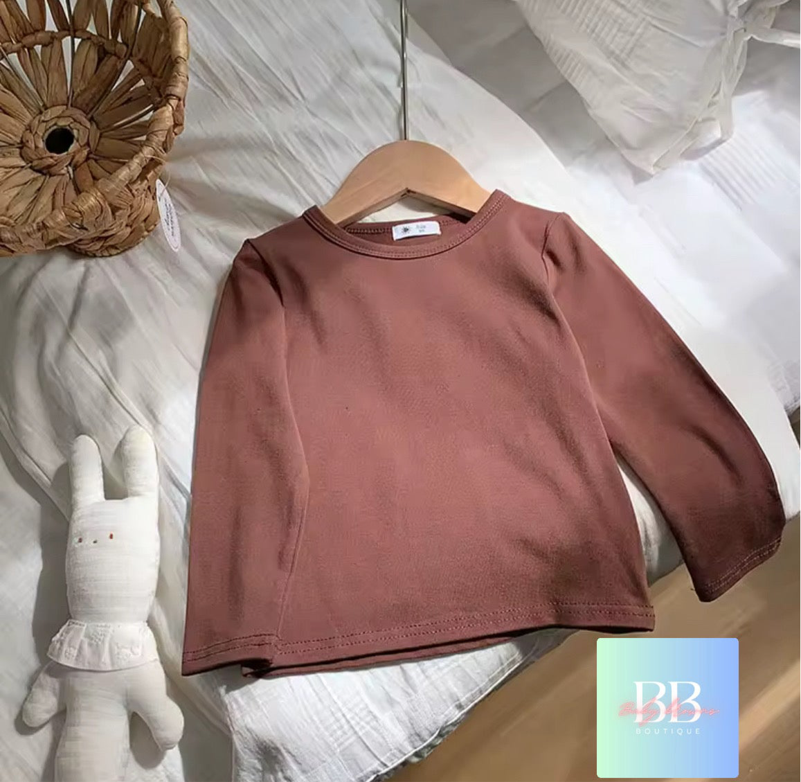 Brown sweatshirt on a hanger with a soft toy and decorative basket in the background