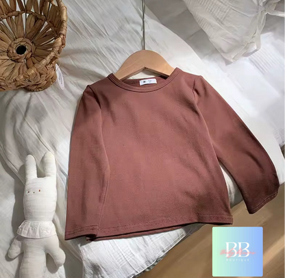 Brown sweatshirt on a hanger with a soft toy and decorative basket in the background