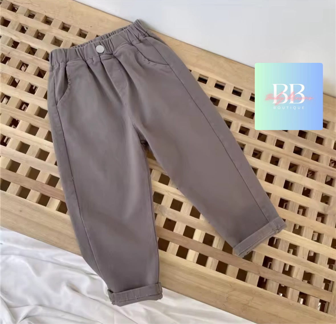 Gray pants on a wooden surface with a brand logo in the corner.