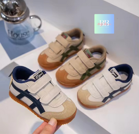 Pair of children's sneakers with a hand holding one shoe on a light background.