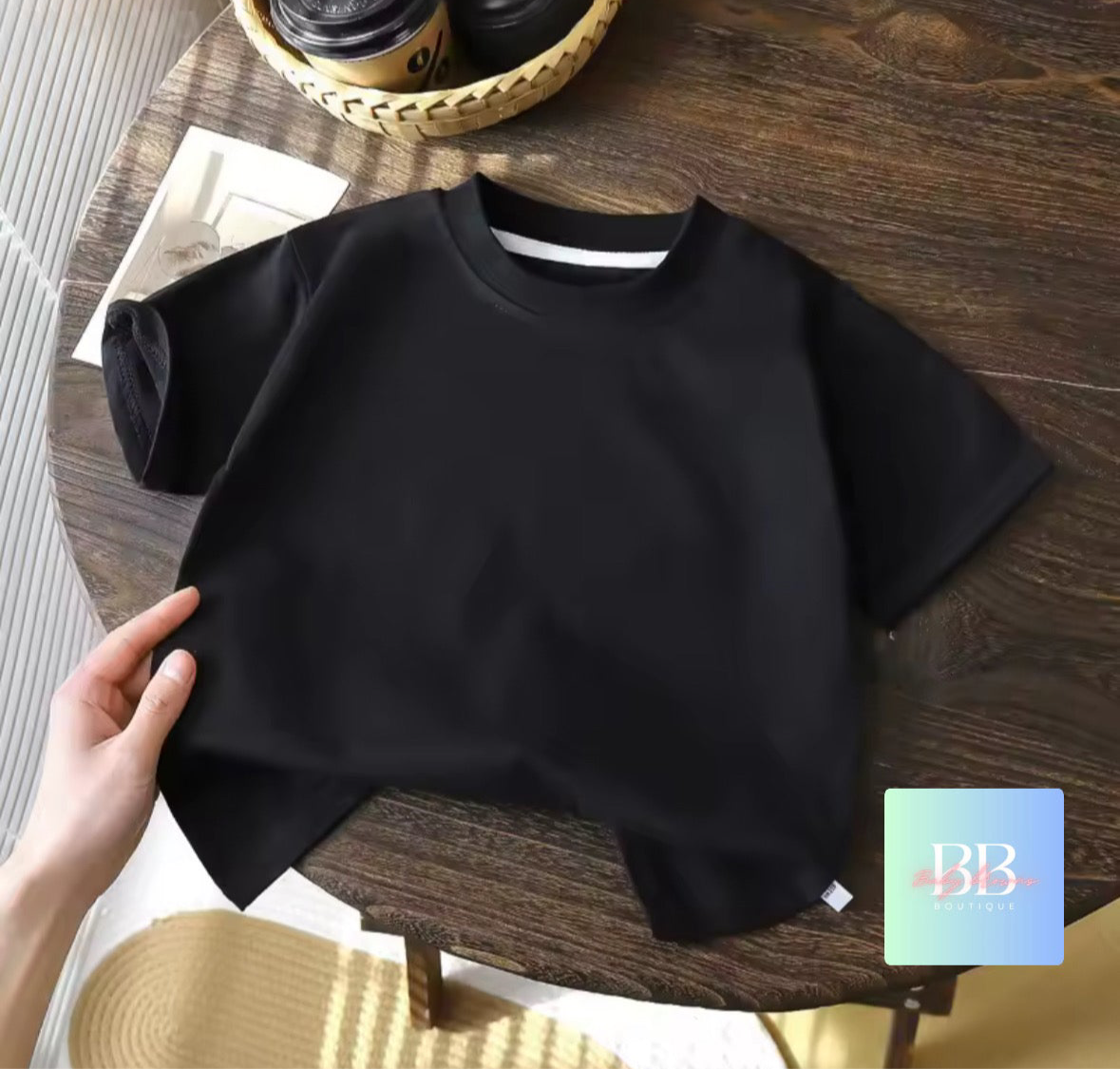 Black t-shirt held by a hand on a wooden table with a blurred background