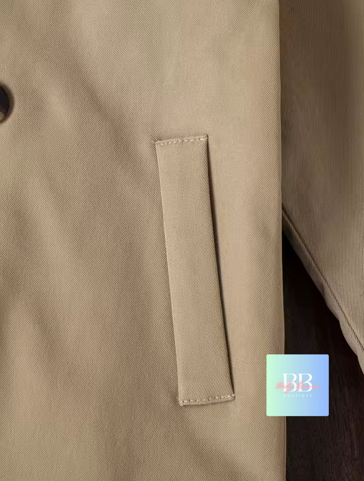 Close-up of a beige coat with a pocket and a brand logo in the corner.