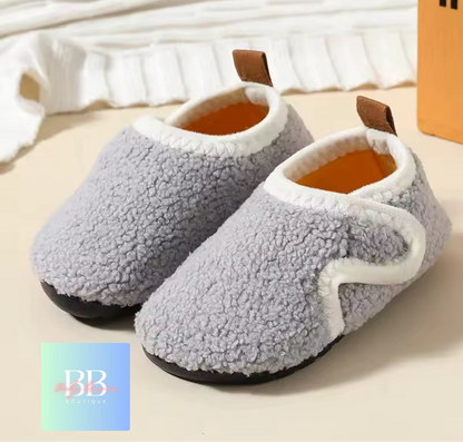 Pair of gray fuzzy slippers on a light background with a brand logo in the corner.