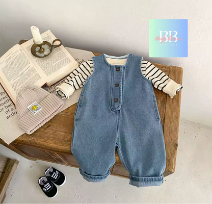 Blue denim overalls on a wooden surface with books and a hat.