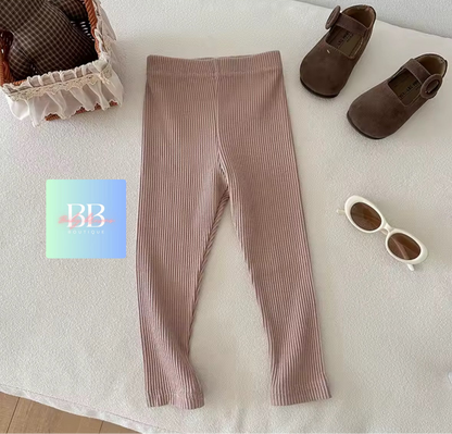 Brown ribbed leggings with baby shoes and sunglasses on a white surface, featuring the brand 'BB'.