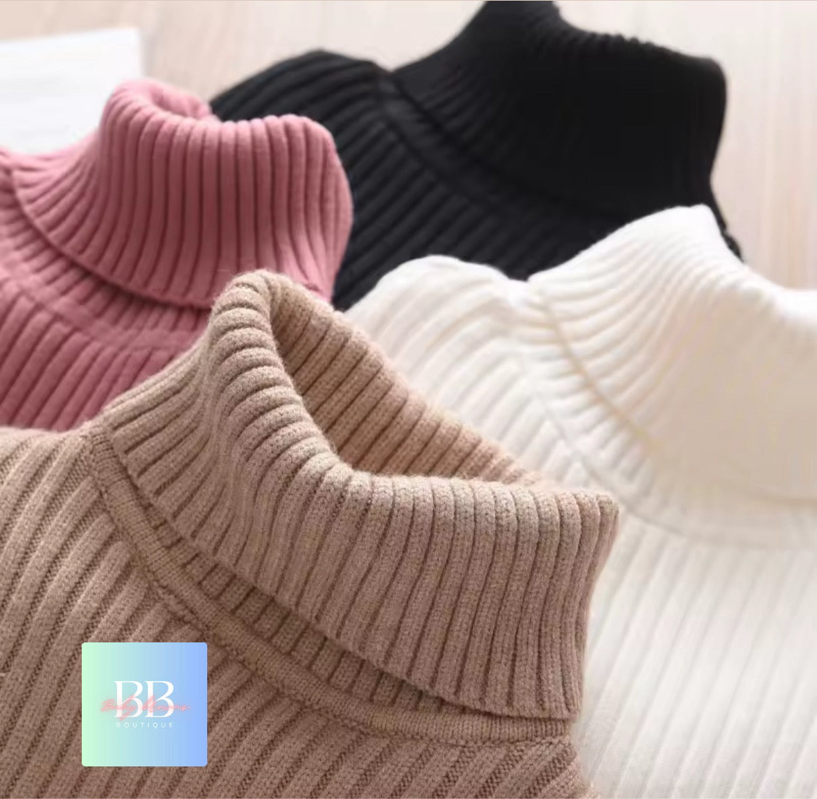 Four knitted turtleneck sweaters in pink, black, beige, and white on a light background.