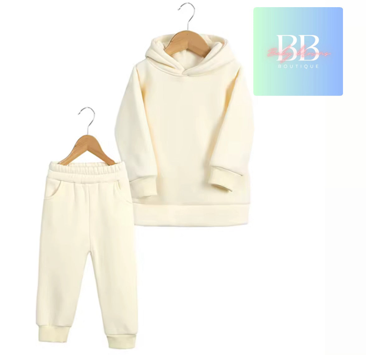 Cream-colored hoodie and pants set on hangers with a brand logo in the corner.