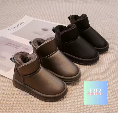 Pair of brown and black children's boots on a textured surface with a magazine underneath.