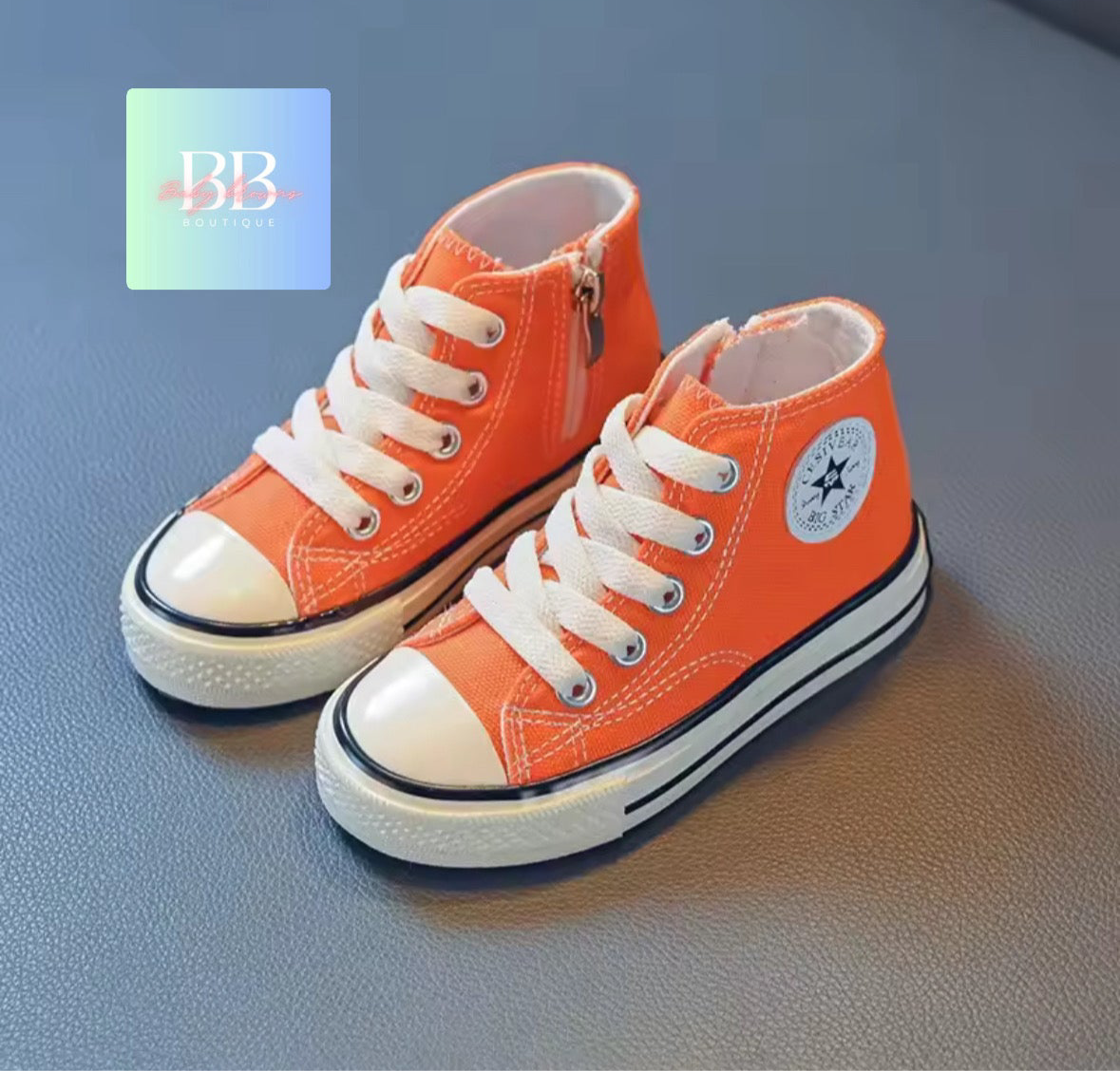 Orange high-top sneakers with white laces on a gray surface, featuring a brand logo in the corner.