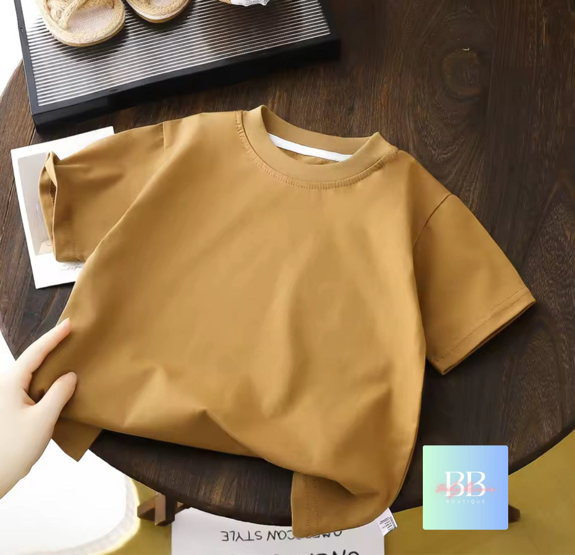 Brown shirt on a wooden table with a hand holding it