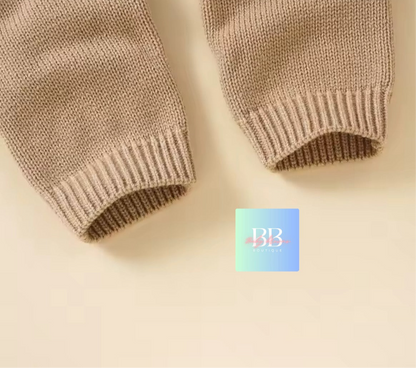 Close-up of beige knitted sleeves on a beige background with a brand logo in the corner.