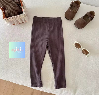 Brown ribbed leggings on a white surface with shoes and sunglasses nearby.