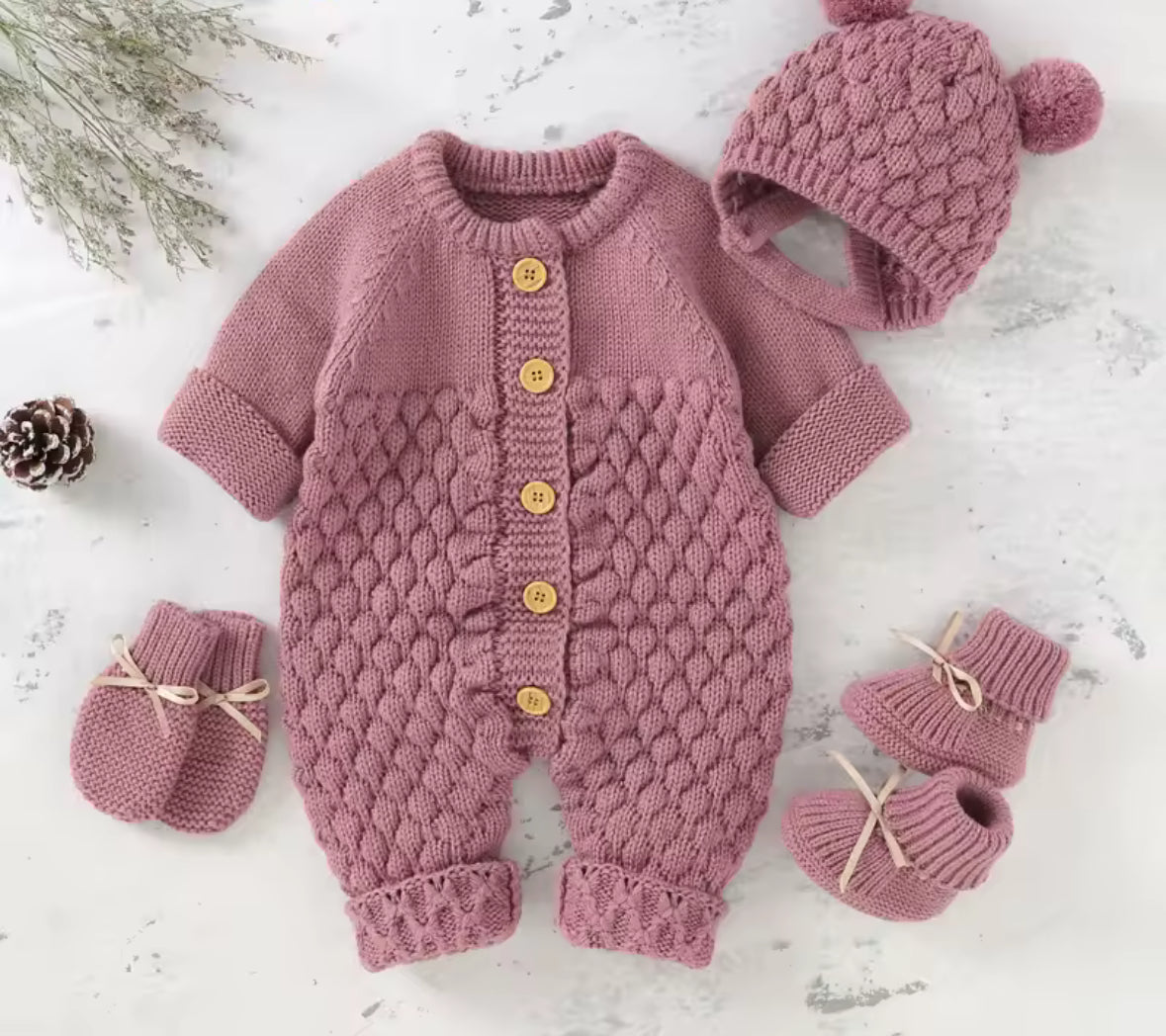 Pink knitted baby outfit with hat, romper, and booties on a light background