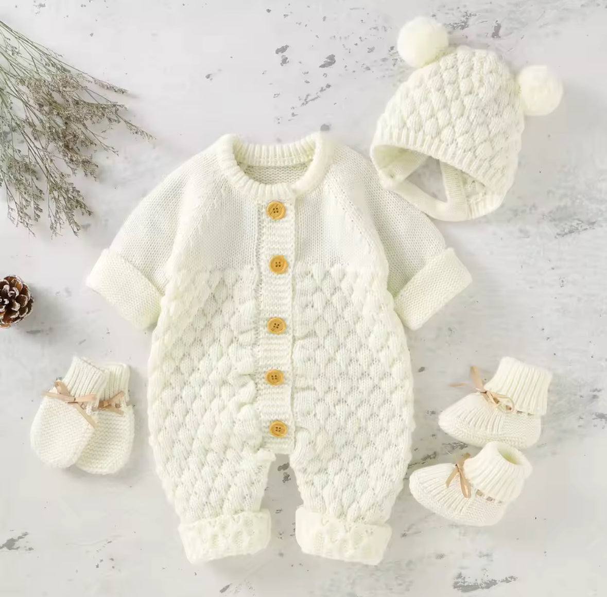 Knitted baby outfit with romper, hat, and booties on a light background