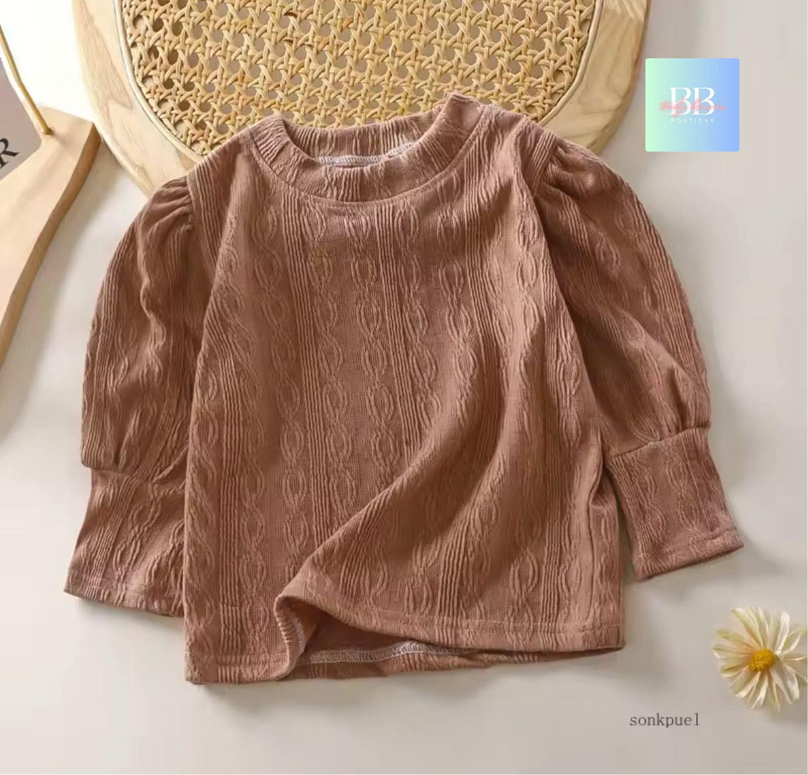 Brown ribbed sweater on a light background with a decorative plate and flower.