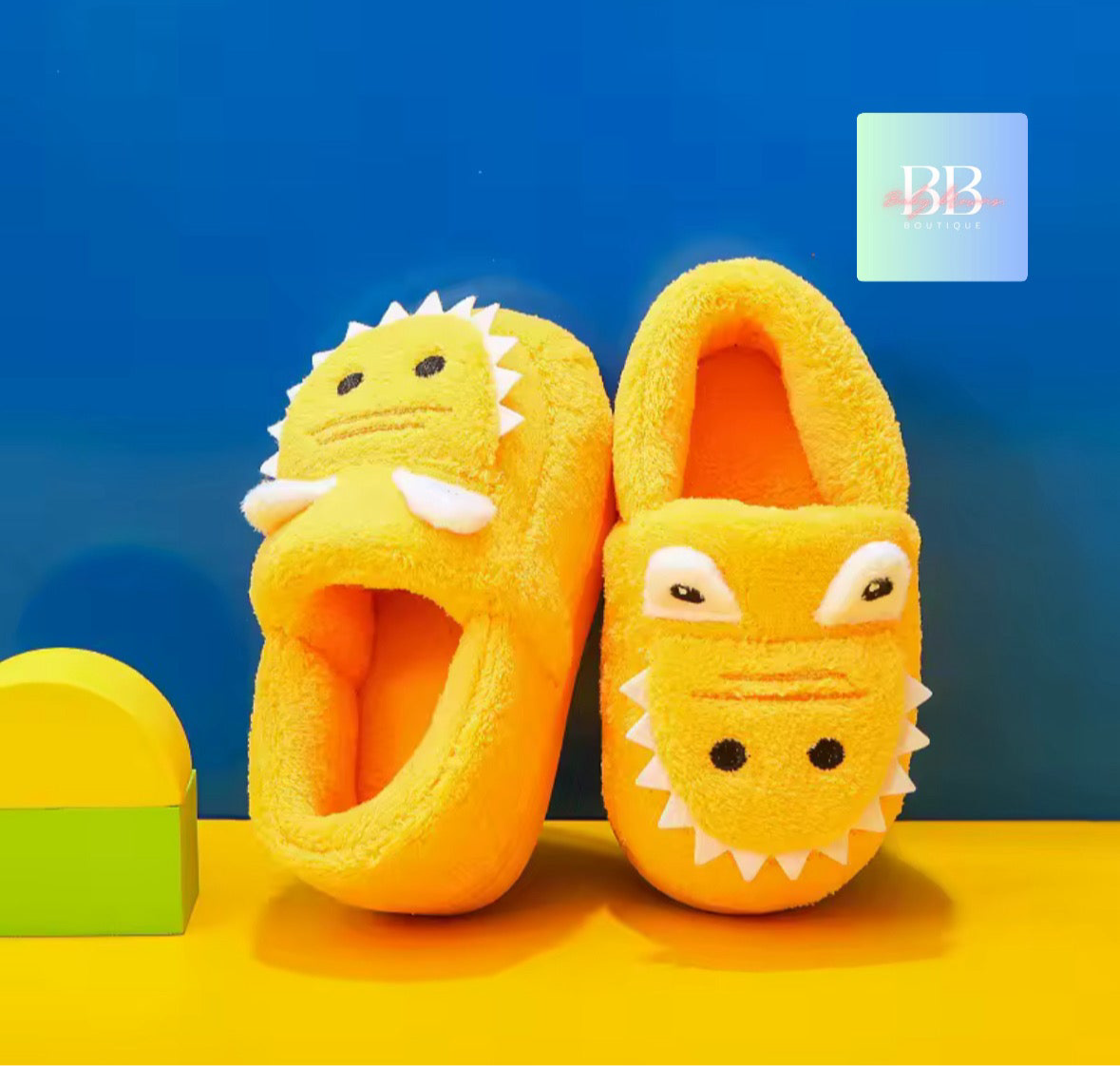 Yellow children's slippers with dinosaur design on a blue and yellow background