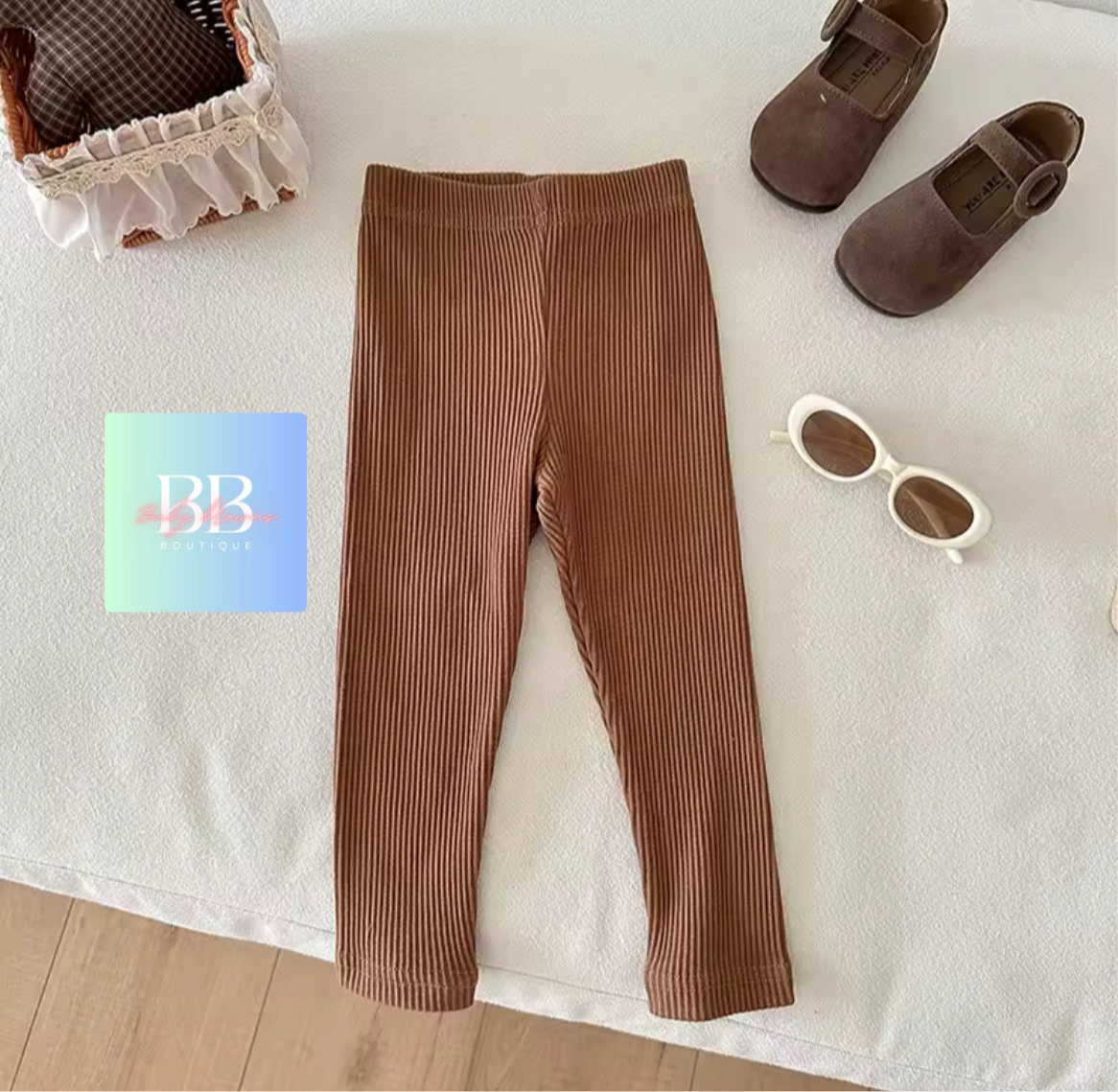 Brown ribbed leggings with shoes and sunglasses on a white surface, featuring a brand logo.