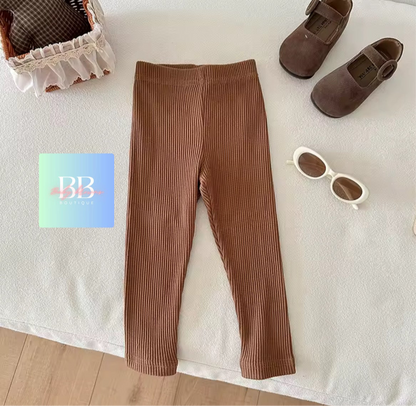 Brown ribbed leggings with shoes and sunglasses on a white surface, featuring a brand logo.
