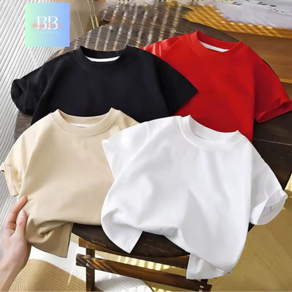 Four plain t-shirts in black, red, beige, and white on a wooden chair.