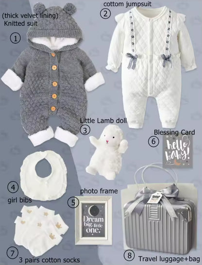 Collection of baby items including a gray knitted suit, white cotton jumpsuit, lamb doll, bibs, photo frame, and travel luggage on a light gray background.