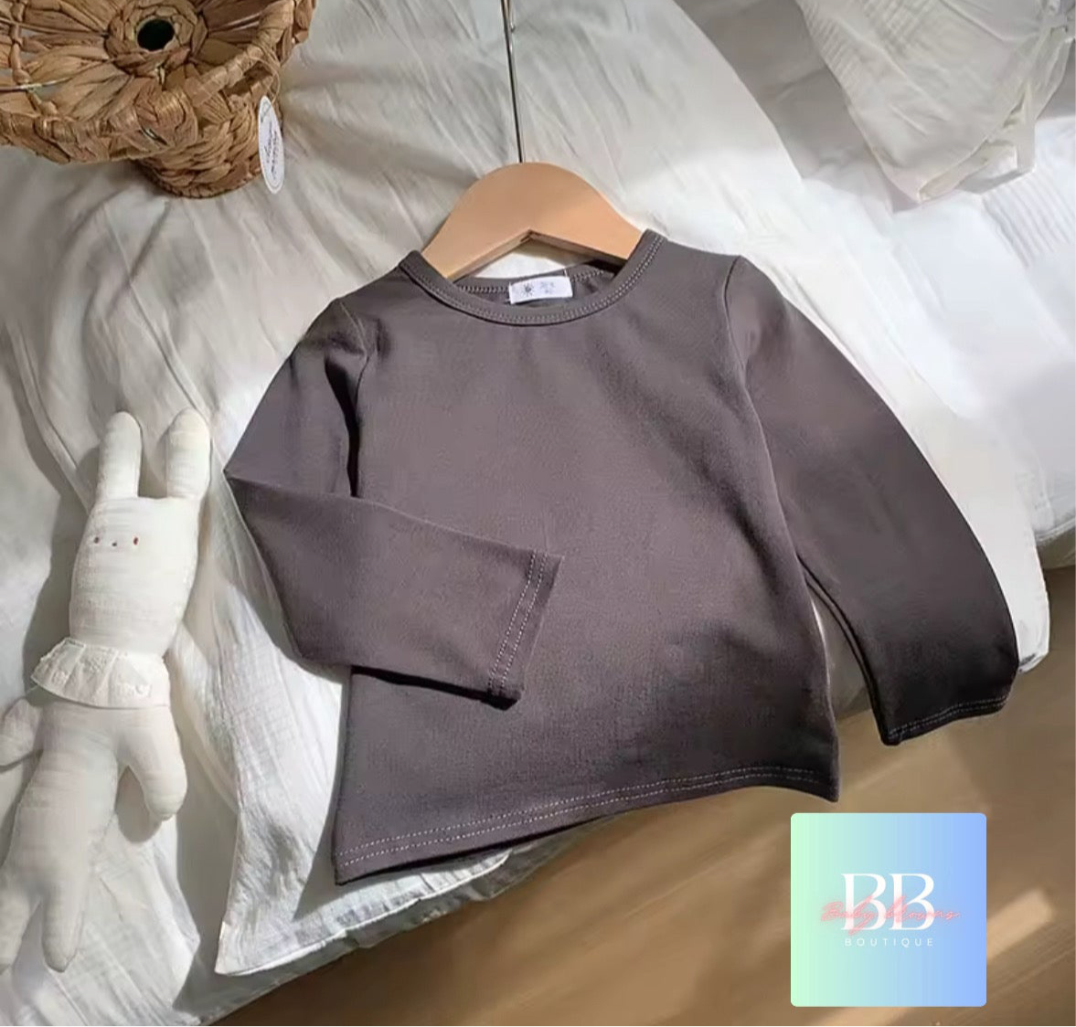 Brown children's sweatshirt on a hanger with a plush toy and woven basket in the background