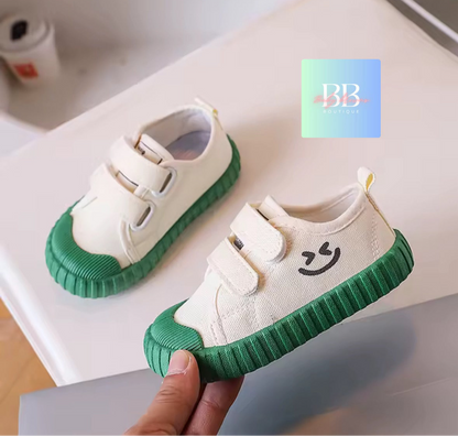 White baby shoes with green soles held by a hand on a light background