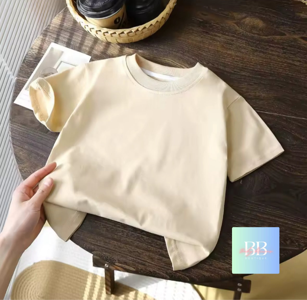 Beige t-shirt on a wooden table with a coffee cup and straw hat in the background